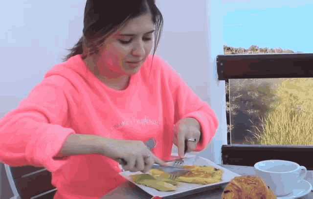 a woman wearing a pink sweater with the word happiness on it is eating a plate of food