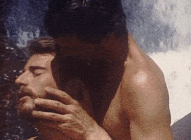 a shirtless man is kissing another shirtless man on the neck