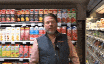 a man in a vest stands in front of a shelf of juices
