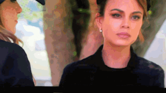 a woman wearing a black hat and earrings is looking at the camera