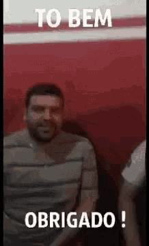 a man in a striped shirt is sitting in front of a red wall and says `` to bem obrigado '' .
