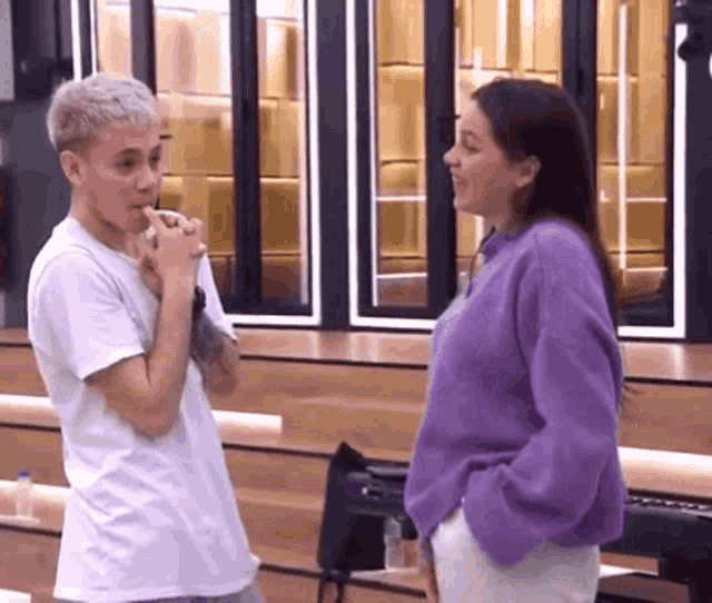 a man in a white shirt and a woman in a purple sweater are talking to each other .