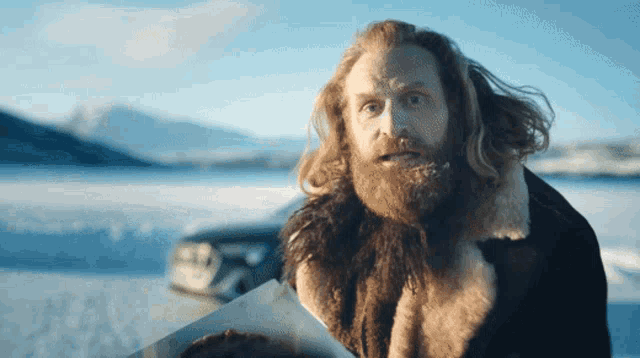 a man with a beard wearing a fur coat stands in the snow