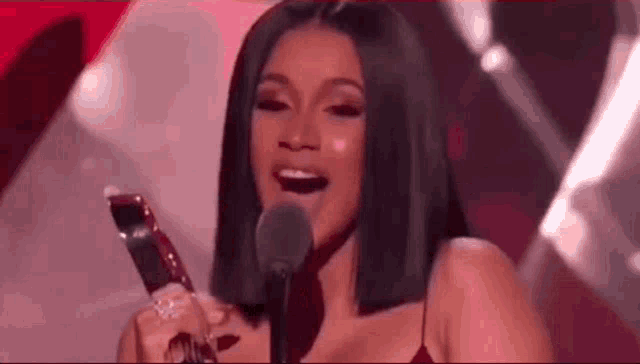 cardi b is holding a trophy and speaking into a microphone on stage .
