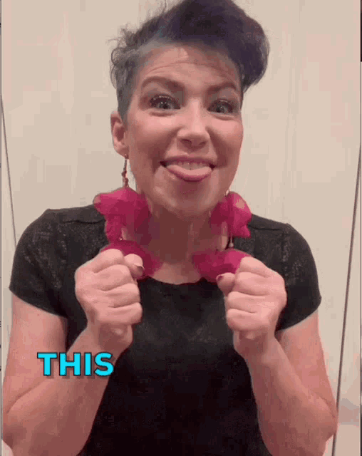 a woman with purple hair is wearing a black shirt and a pink necklace with the word this written in blue