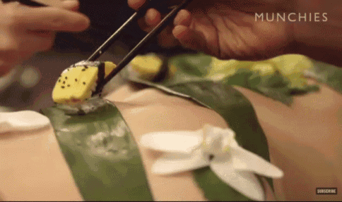 a person is eating sushi on a woman 's back with chopsticks