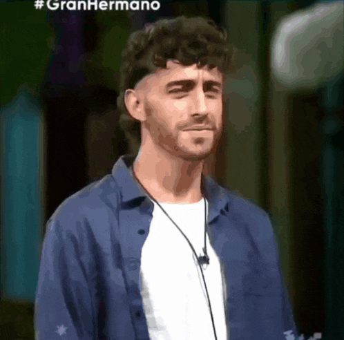 a man wearing a blue shirt and a white t-shirt is standing in front of a sign that says #gran hermano