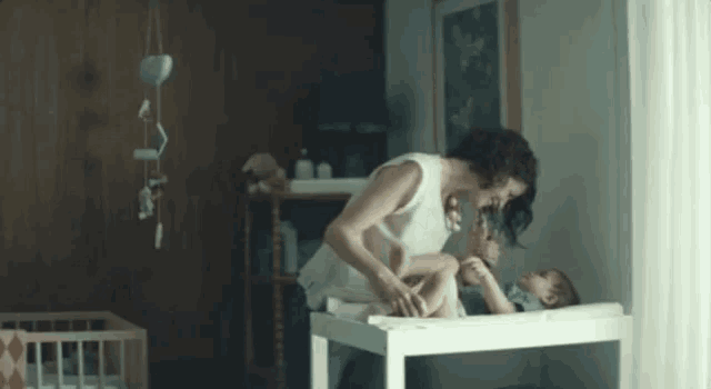 a woman is changing a baby 's diaper on a changing table in a nursery .