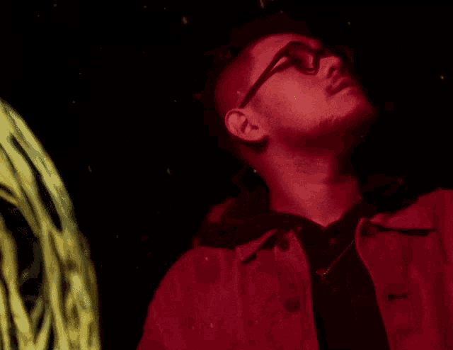 a man wearing glasses and a red jacket looks up into the sky