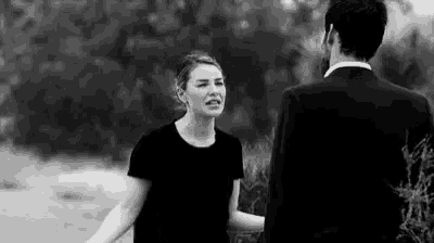 a man in a suit and a woman in a black shirt are standing next to each other in a black and white photo .