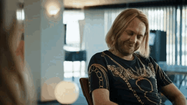 a man with long blonde hair is wearing a black shirt with chains on the sleeves