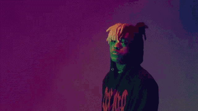 a man wearing a hoodie with dreadlocks is standing in front of a purple background .