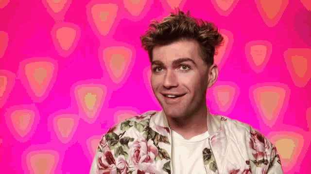 a man wearing a floral jacket is smiling on a pink background