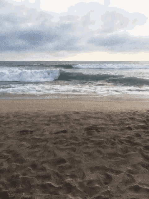 a sandy beach with waves coming in and a cloudy sky