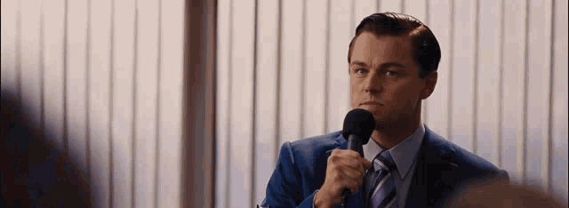 a man in a suit and tie is holding a microphone in front of a window .