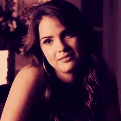 a woman with long brown hair and hoop earrings is looking at the camera .