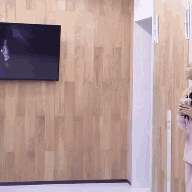 a woman stands in front of a wooden wall with a flat screen tv hanging on it