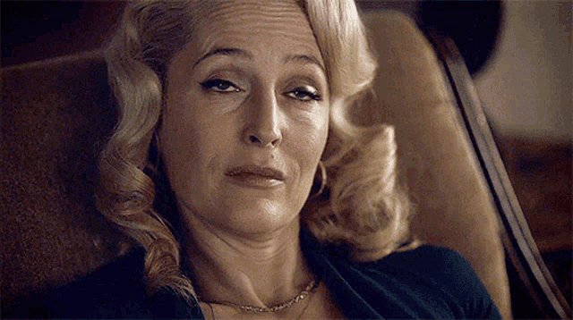 a woman is sitting in a chair with her eyes closed and a necklace on her neck .