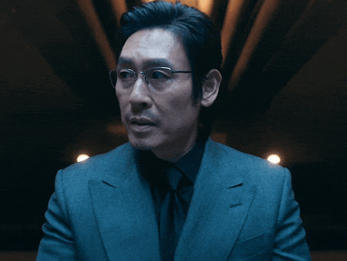 a man with glasses and a suit looks at the camera