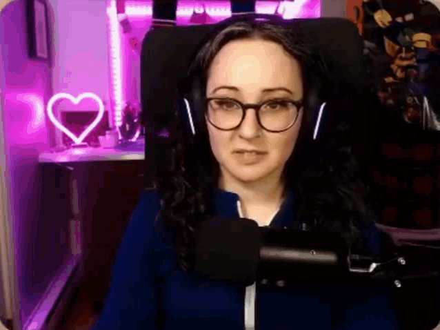 a woman wearing glasses and headphones is sitting in front of a microphone in a recording studio .
