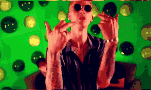 a man wearing sunglasses is giving the middle finger in front of a green background