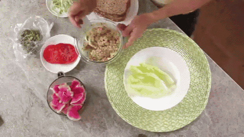 a person is making a sandwich with lettuce , tomatoes , and a bowl of food .