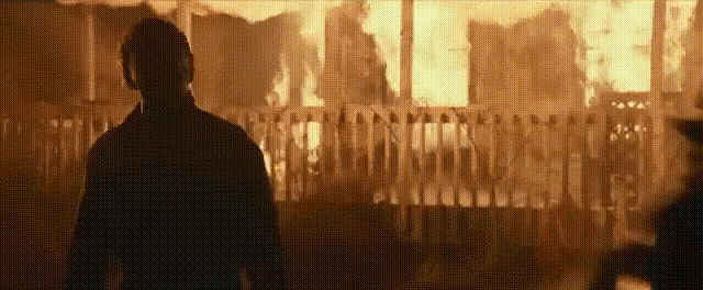 a man is standing in front of a burning house in a dark room .