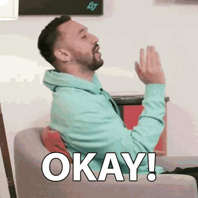 a man in a green hoodie is sitting in a chair and says okay