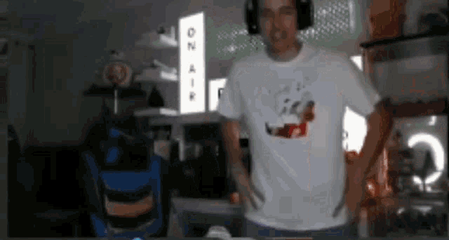 a man wearing headphones and a white t-shirt is standing in front of a sign that says on air .