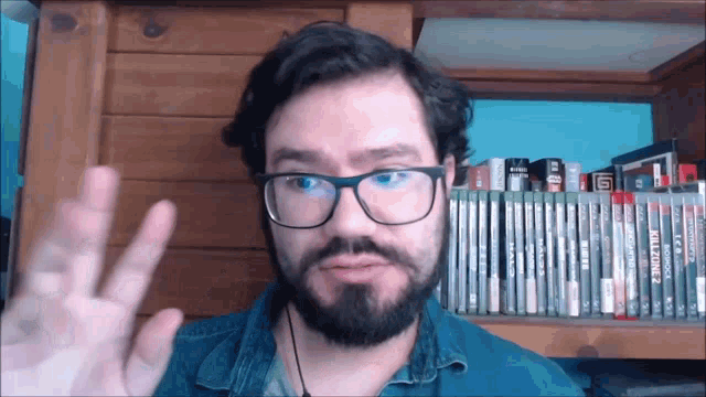 a man with glasses and a beard is giving a peace sign in front of a shelf full of dvds