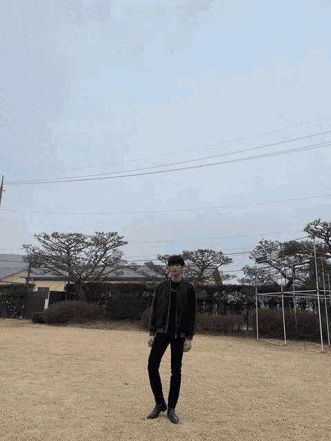 a man in a black jacket is standing in a field with trees in the background