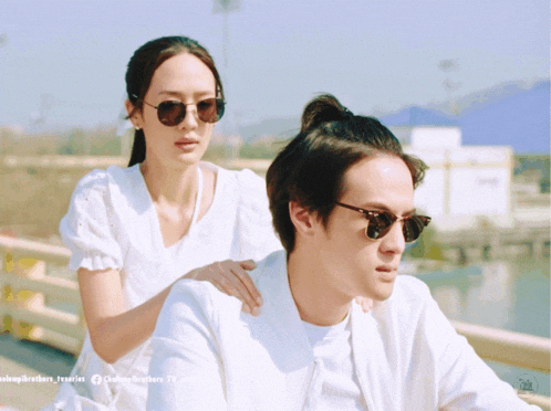 a woman is putting her hand on a man 's shoulder while a man wearing sunglasses looks on