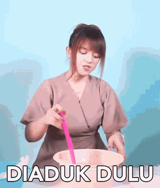 a woman is mixing something in a bowl with a pink spoon and the words diaduk dulu written on the bottom .