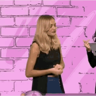 a woman is standing in front of a pink brick wall with her hands together .