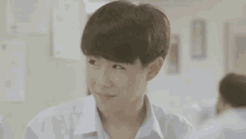a young boy in a school uniform is sitting in a classroom and making a funny face .