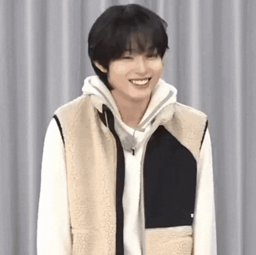 a young man wearing a sherpa vest and a white hoodie is smiling .