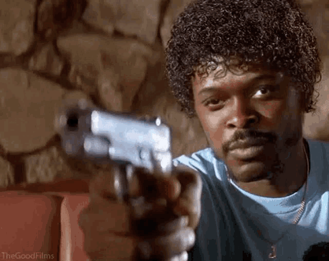 a man with curly hair and a mustache is holding a gun and pointing it at the camera .