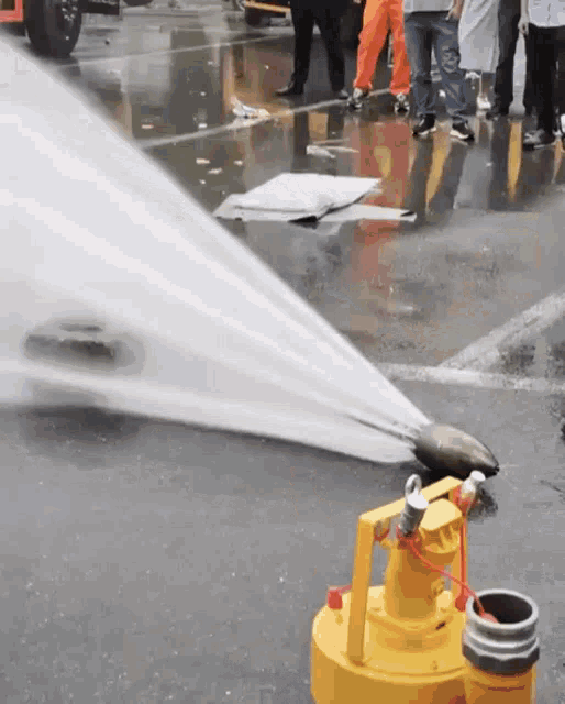 a group of people standing around a yellow hose spraying water