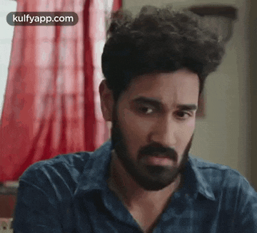 a man with a beard and curly hair is sitting in front of a window .