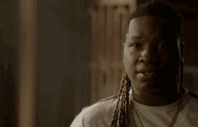 a man with dreadlocks is wearing a white shirt and a gold necklace