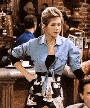 a woman in a blue shirt and a black and white dress is standing in front of a man in a restaurant .