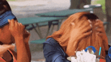 two women are sitting next to each other and one of them is covering her eyes with her hand .
