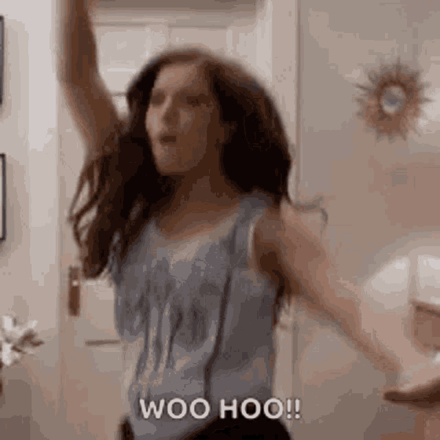 a woman is dancing in a room with her arms in the air and saying woo hoo .