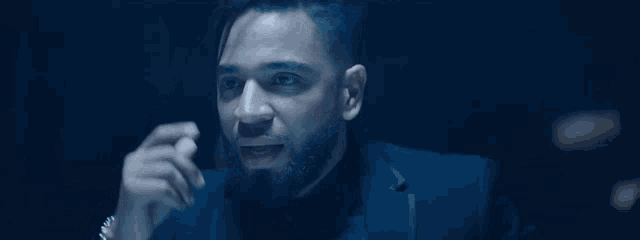 a man with a beard and a suit is talking on a cell phone in a dark room .