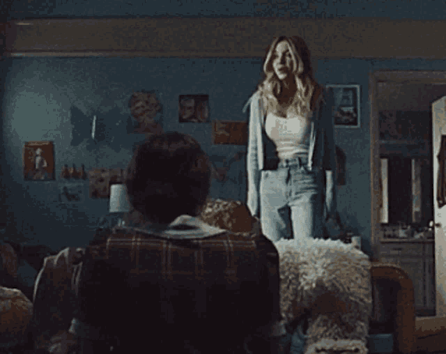 a woman is standing in a room with a man sitting on a couch .