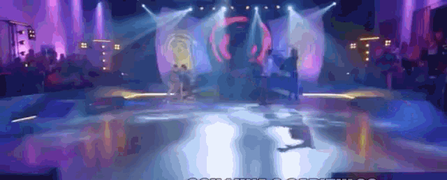 a group of people dancing on a stage with purple lights