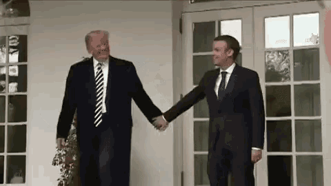 two men in suits are shaking hands in front of a window .
