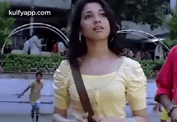 a woman in a yellow shirt is standing in front of a fountain and looking up at the sky .