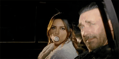a woman blowing a bubble gum next to a man with a beard