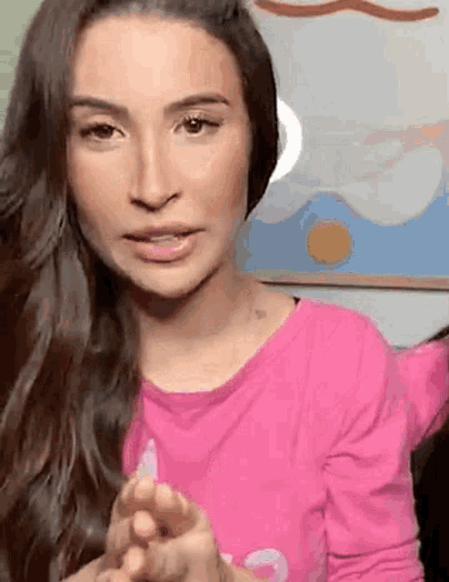 a woman with long hair is wearing a pink shirt and holding her hands together .